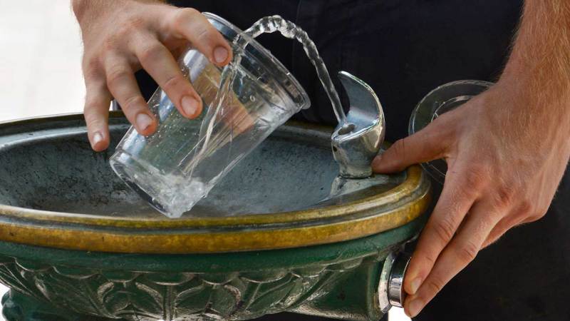 A close up on a drinking fountain, with a person filling a cup with water.